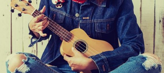 This is a shot of a torso in a denim outfit and playing the guitar.