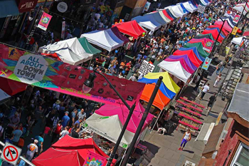 This is a photo of the All About Downtown street festival that happens every year in September. It is a very crowded street of peopl, tents and a street banner with the festivals name on it.
