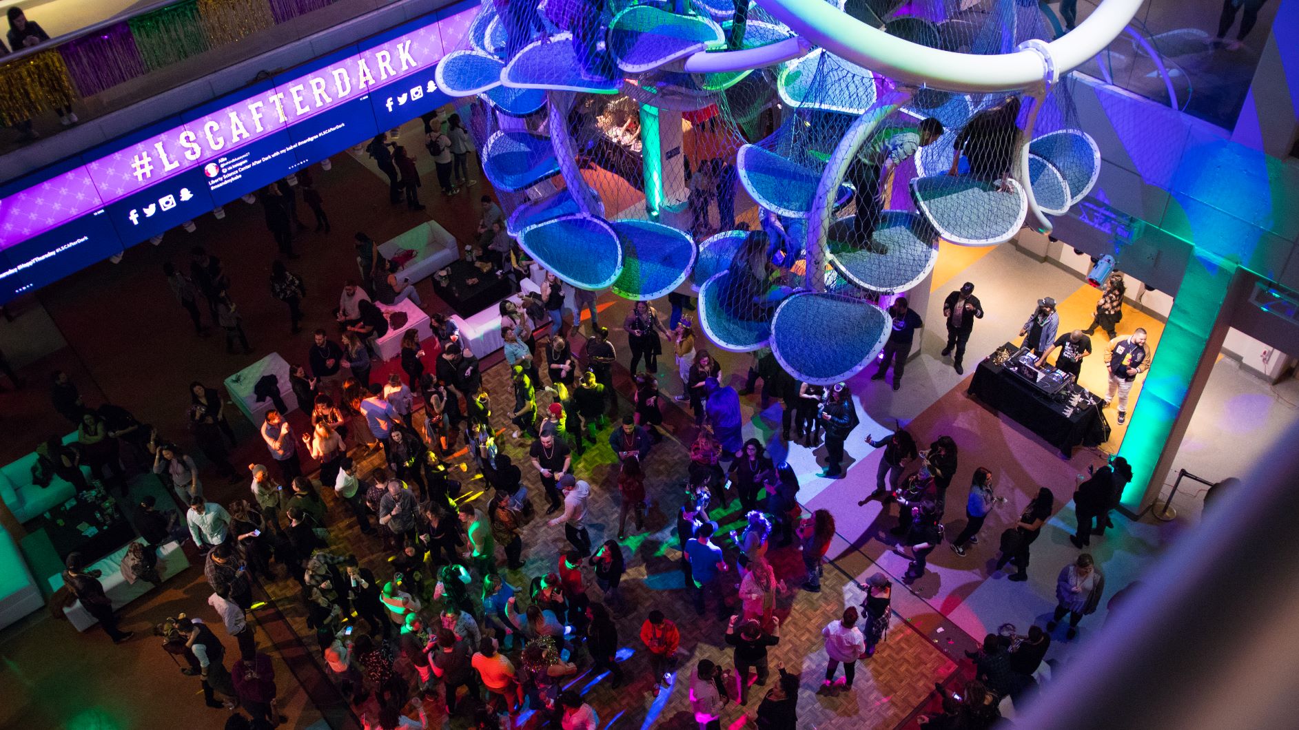 Overhead view of the LSC AfterDark crowd below that is lined with dancers dj and seating areas with white sofas.