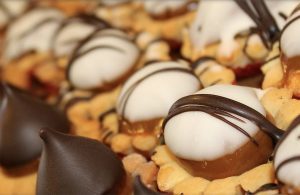 Picture of rows of cookies topped with hershey kisses and otheres that are topped with marshmallows and drizzled with chocolate.