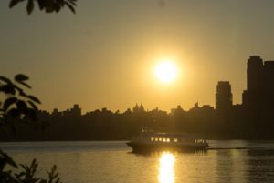 With a city background shadow the hackensack riverkeeper boat is on the water at sunset.