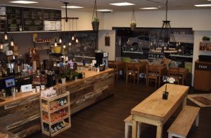 Inside of a trendy cafe with wood table with benches, lighting fixtures, plants, and chalk board signs.