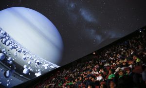 Interior view of stadim seating in the liberty science center plantetarium looking up to a screen with a large planet displayed on the dome.