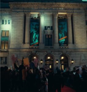 A historical building labeled Wayne hall and crowd commotion in front of the building with police at the head of the red carpet stairs.