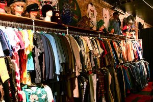 Interior shot of a vintage store showing one wall that has stacked clothing bars and a shelf with props above with mannequin heads with hats and tshirts hanging on the walls.