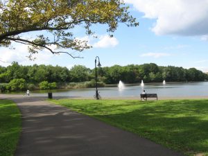 Sunny day in North Hudson Park overlooking a lake with man sitting on bench watching the water spouts.