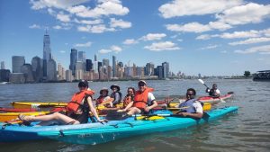 group of people kayaking on the river with the Manhattan skyline in the background