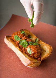 Meatball sub being garnished with basil