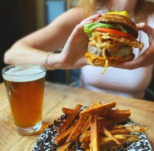 woman holding a burger over a plate of fries and glass of beer