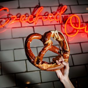 hand holding up a pretzel under a neon sign that reads "czeched out"