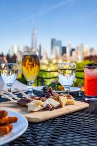 glasses of various drinks and cocktails with an appetizer, the Manhattan skyline can be seen beyond