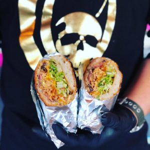 Man holding up a burrito cut in half showing the camera what's inside