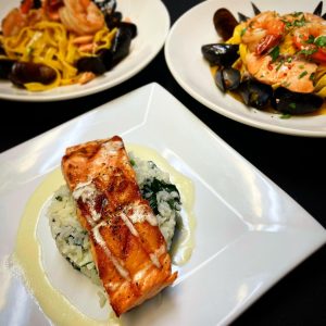 Three plates of various entrees including salmon and mashed potatos and pasta with mussels