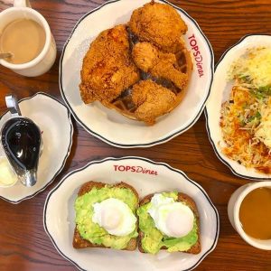 Plates of chicken and waffles, avocado toast with two mugs of coffee