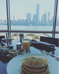 stack of pancakes on a dining table near a large window overlooking the waterfront and the Manhattan skyline