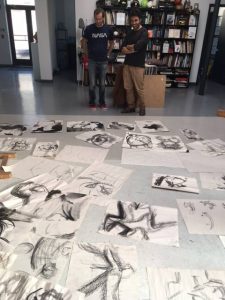 2 men looking at sketches arranged on the floor