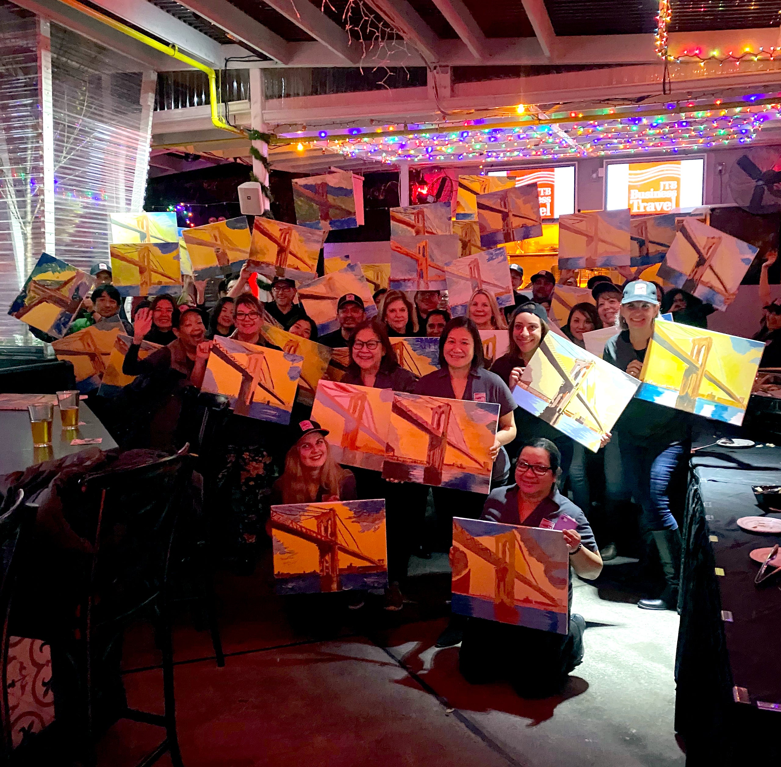 group of people holding up their finished paintings at a painting party