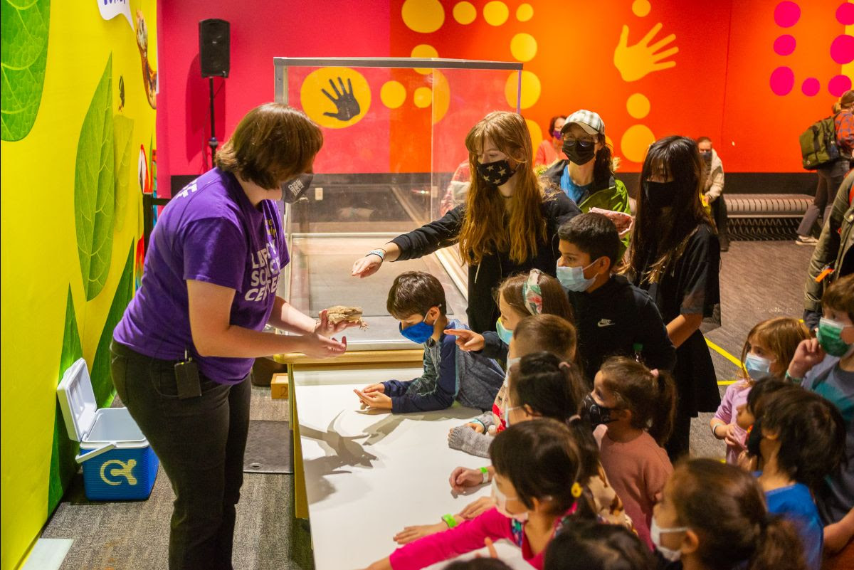 An image of children gathered around an employee at the Liberty Science Center, as they are teaching about interactive learning and getting the kids excited about science. 