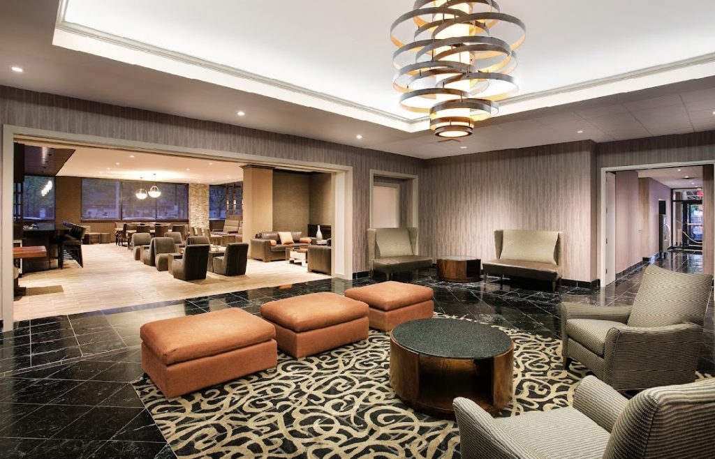An image of the lobby area at the DoubleTree by Hilton Hotel & Suites in Jersey City, NJ, where the room is filled with trendy seating and lighting fixtures