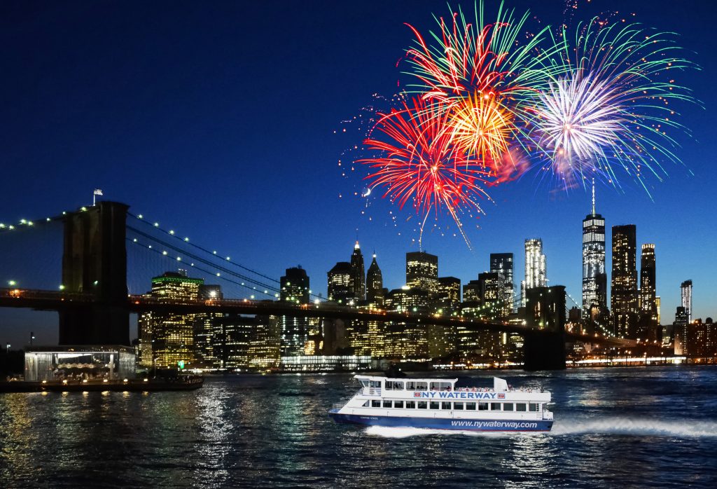 Nighttime image of the Hudson River and the NY skyline in the background, with fireworks going off in the distant sky for the 4th of July