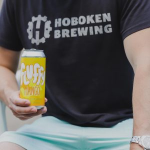 Man wearing black tshirt that says "Hoboken Brewing" and holding a yellow can 