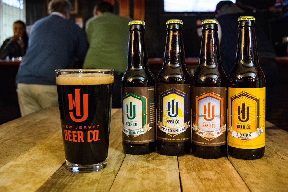 glass of beer next to 4 bottles of beer, all with labeled "New jersey Beer Co." and their logo