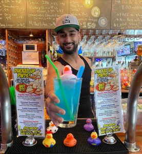 man raising blue cocktail with a rubber ducky in font of two flyers for "Ducked up Pints"