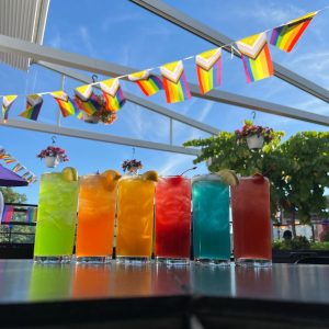 Row of colorful cocktails under a rainbow flag bunting