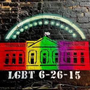 spray painted tag on a black brick wall; tag is an a image a rainbow white house with "LGBT 6-26-15" below