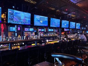 Sports bar with 6 large flat screen TVs on the wall along the length of the bar