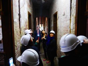 Group of people with white hard hats on touring an old hospital complex