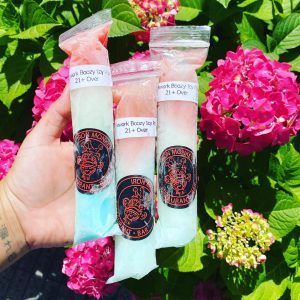 Hand holding 3 rainbow alcoholic ice pouches over some flowers