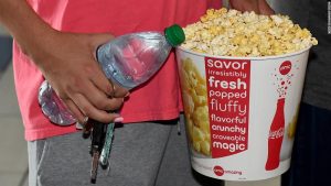 person holding bottled water in one hand and movie theatre bucket of popcorn in the other