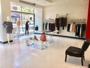 Inside Alba boutique; white tile floors with two tables of products, three clothing racks on the wall as well as some manequins
