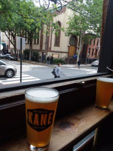 glass of beer with "Brewing Kane" on the side near the window