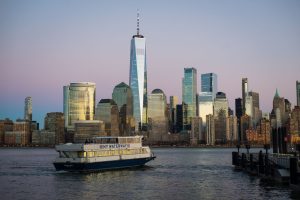 Riverfront view at dusk with buildings in the background and cruise ships sailing along the New York Waterway