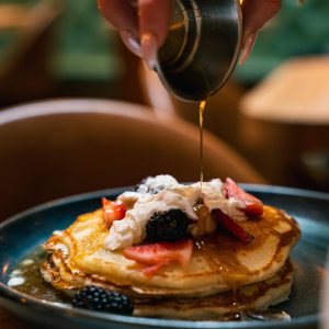 syrup pouring onto a stack of pancakes topped with fruit