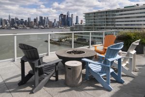 Riverfront view with chairs at Port Imperial, with outdoor patio around a firepit and view of the New York Waterway