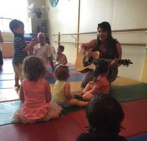 children sitting around a woman playing guitar