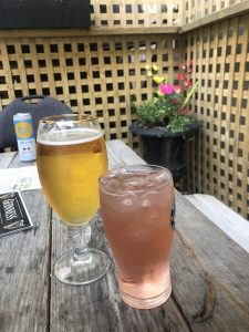 A light pink colored drink in a tall glass next to to a glass goblet of beer