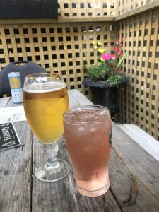 A light pink colored drink in a tall glass next to to a glass goblet of beer