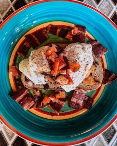 Plate of toast topped with over easy eggs chopped tomatoes and bacon