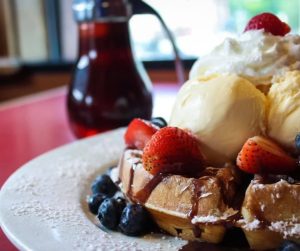 waffles with fruit and ice cream next to pitcher of syrup