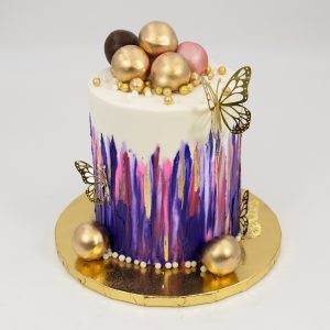 decorative drip cake with butterflies on the sides and topped with gold balls 