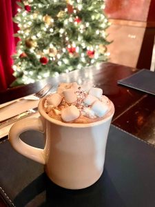 Cup of hot coco with Christmas tree in the background at Carpe Diem in Hudson County, NJ