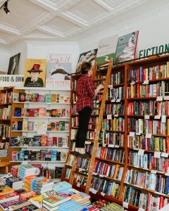 woman on a shelf ladder browsing books in a bookstore