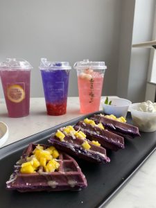 long plate of purple/taro flavor waffles next to three colorful drinks in to go cups