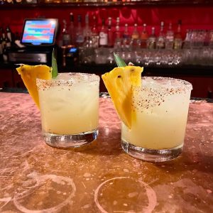 two cocktails with pineapple wedges on a bar counter top