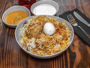 Plate of chicken briyani and two bowls of extra sauces 